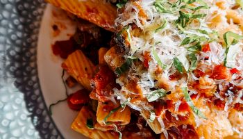A plate of rigatoni pasta in spicy tomato sauce, topped with grated cheese, basil, and herbs.