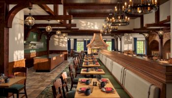A stylish restaurant interior with long wooden tables, cushioned booths, warm lighting, chandeliers, and arched windows.