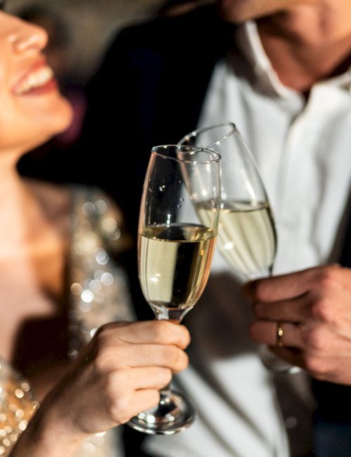 A couple toasting with champagne flutes at a formal event, smiling and dressed up for a celebration.