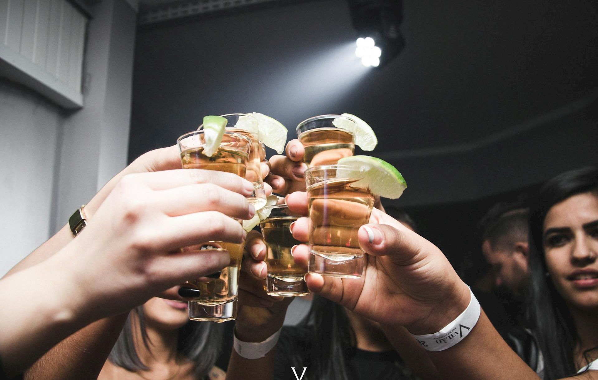 A group of people clinks shot glasses with lime wedges, celebrating together at a party or night out.