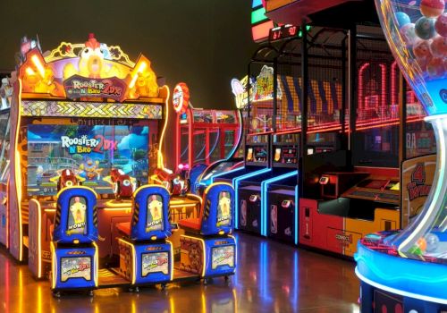 A bright arcade with glowing crane and basketball games, colorful prizes, and neon rides lining the arcade floor.