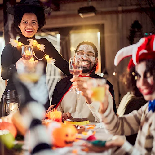 A smiling woman and man toast with glasses at a lively indoor party, with warm lights and friends celebrating.